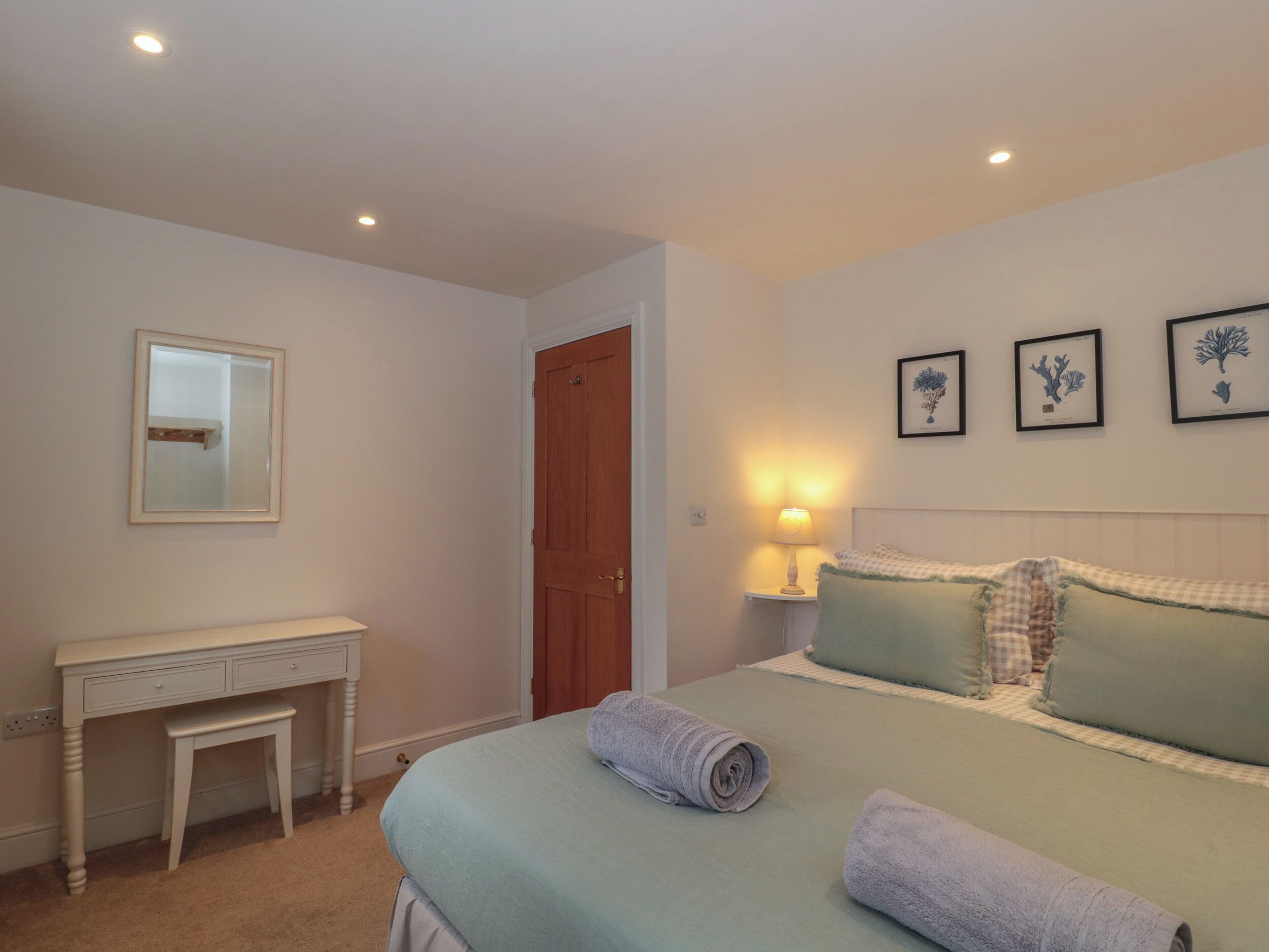 A bedroom with a bed, a bedside table, a mirror, and a door.