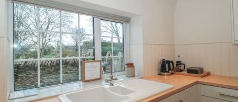 Une cuisine moderne dotée d’une grande fenêtre, de meubles blancs et d’un plan de travail sur lequel se trouvent une bouilloire et un grille-pain.