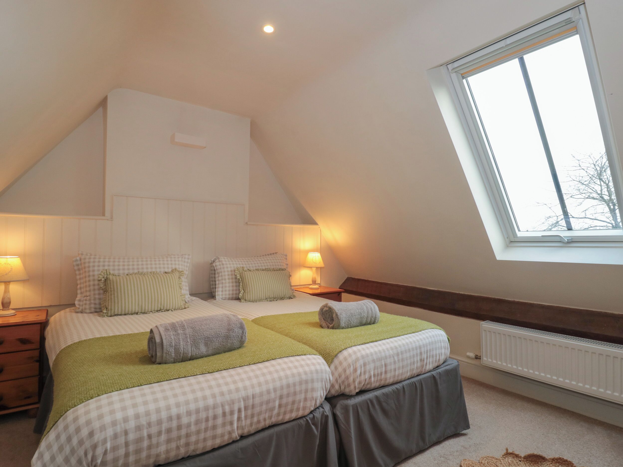 A bedroom with two beds, a sloped ceiling, a skylight, and a radiator.
