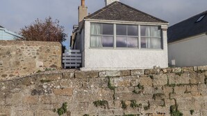 A small, white house with a grey roof, a chimney, and a window with curtains.
