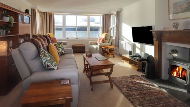 A cozy living room with a fireplace, a sofa, a television, and a view of the water outside.