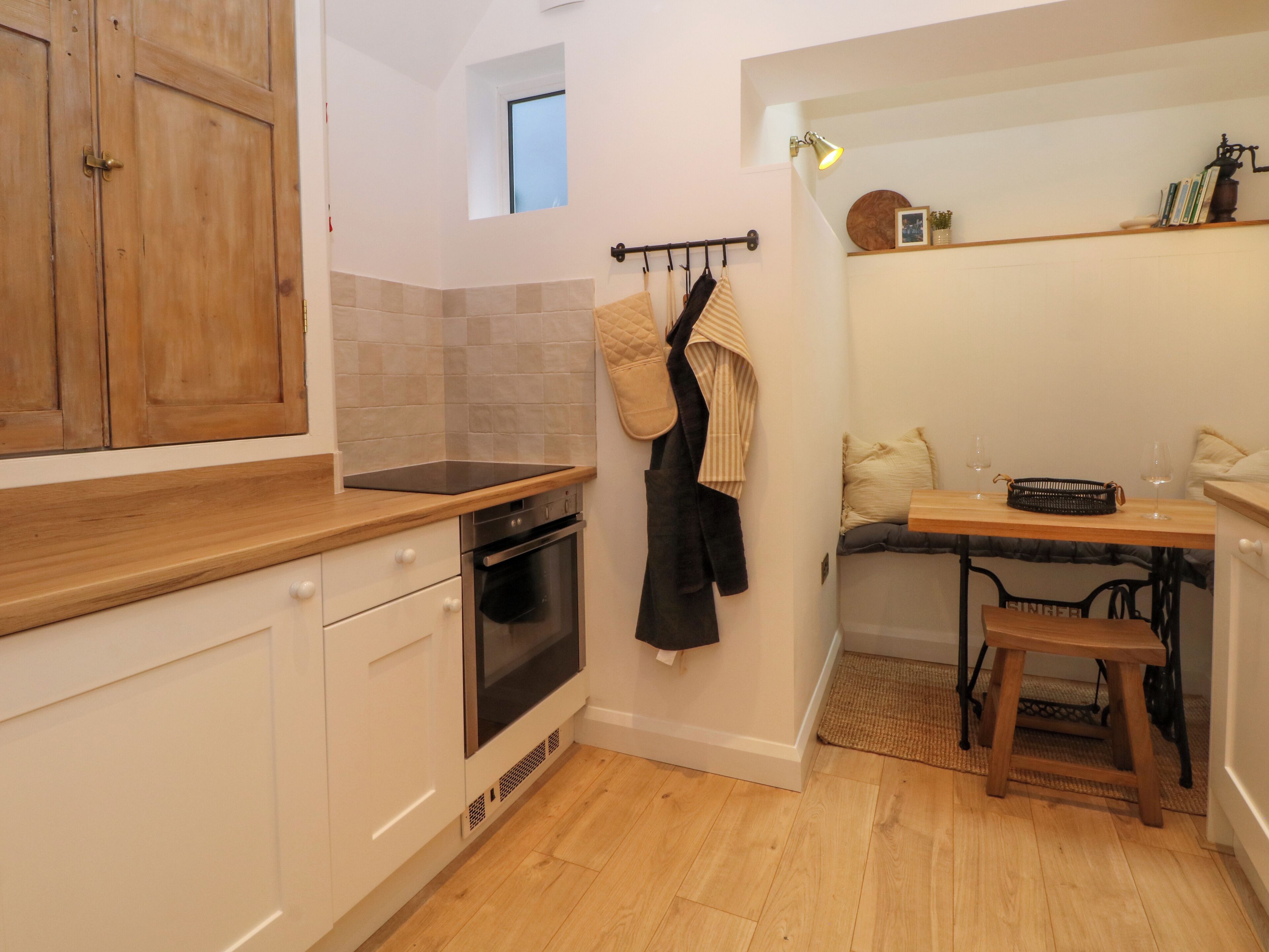 Cocina compacta con armarios de madera, horno empotrado y un pequeño comedor con banco y mesa.