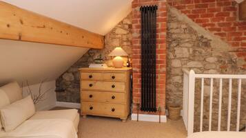 A cozy bedroom with a sloped ceiling, a wooden dresser, a lamp, a radiator, and a crib.