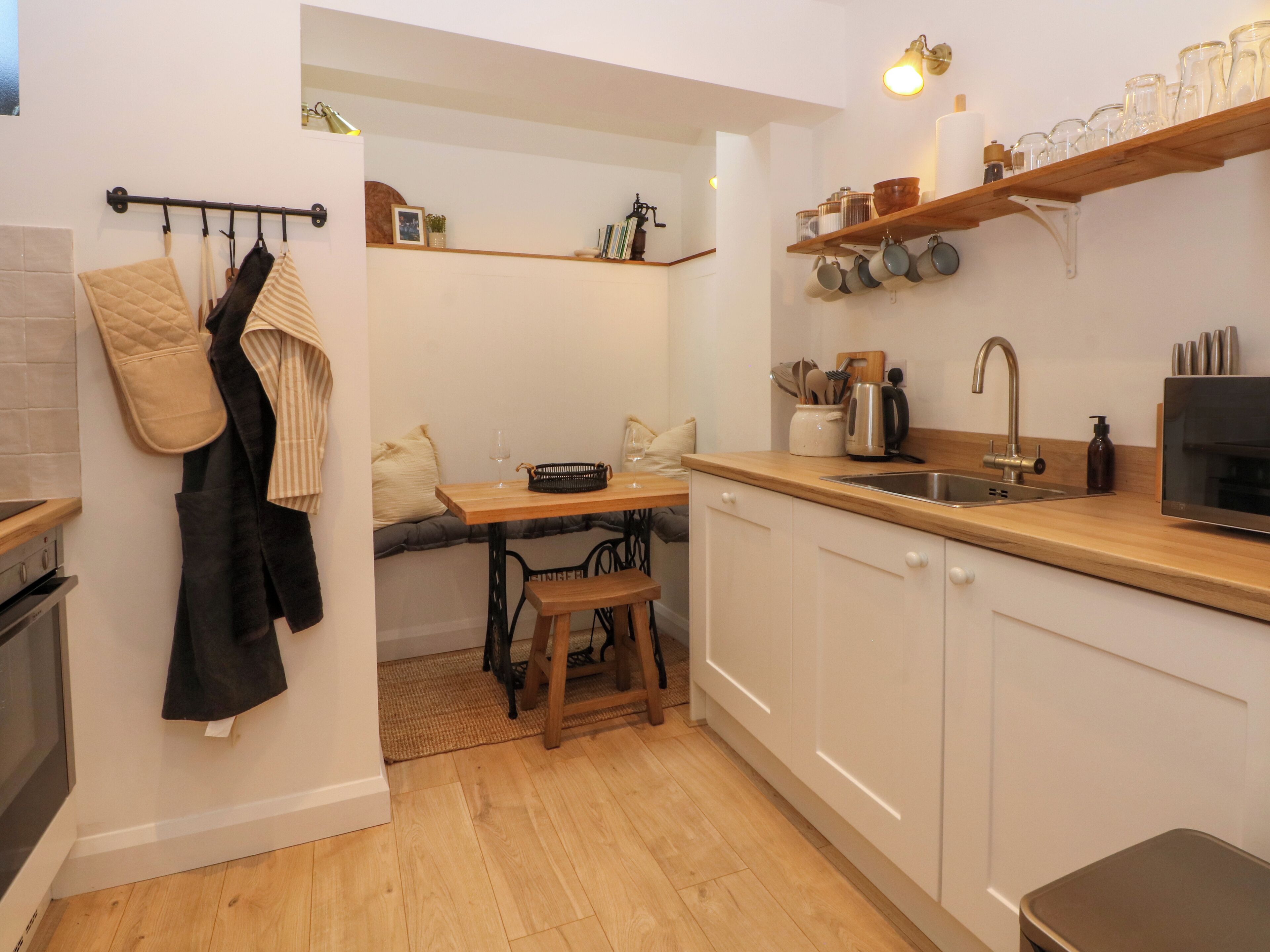A compact kitchen with a wooden countertop, a sink, and a stove. There is a dining area with a bench and a table.