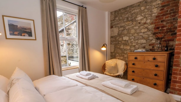 Una cama bien hecha con sábanas blancas, un aparador de madera y una pared de piedra.
