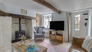 A cozy living room with a fireplace, a television, a sofa, and a table with a magazine and mugs. - Amy Cottage (Wareham)