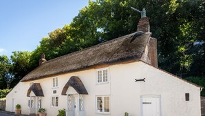 A traditional white building with a thatched roof, multiple windows, and a door. - Amy Cottage (Wareham)