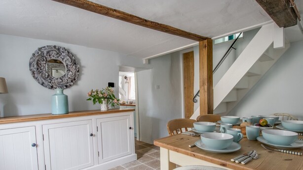 A kitchen with white cabinets, a wooden dining table, and a staircase. - Amy Cottage (Wareham)
