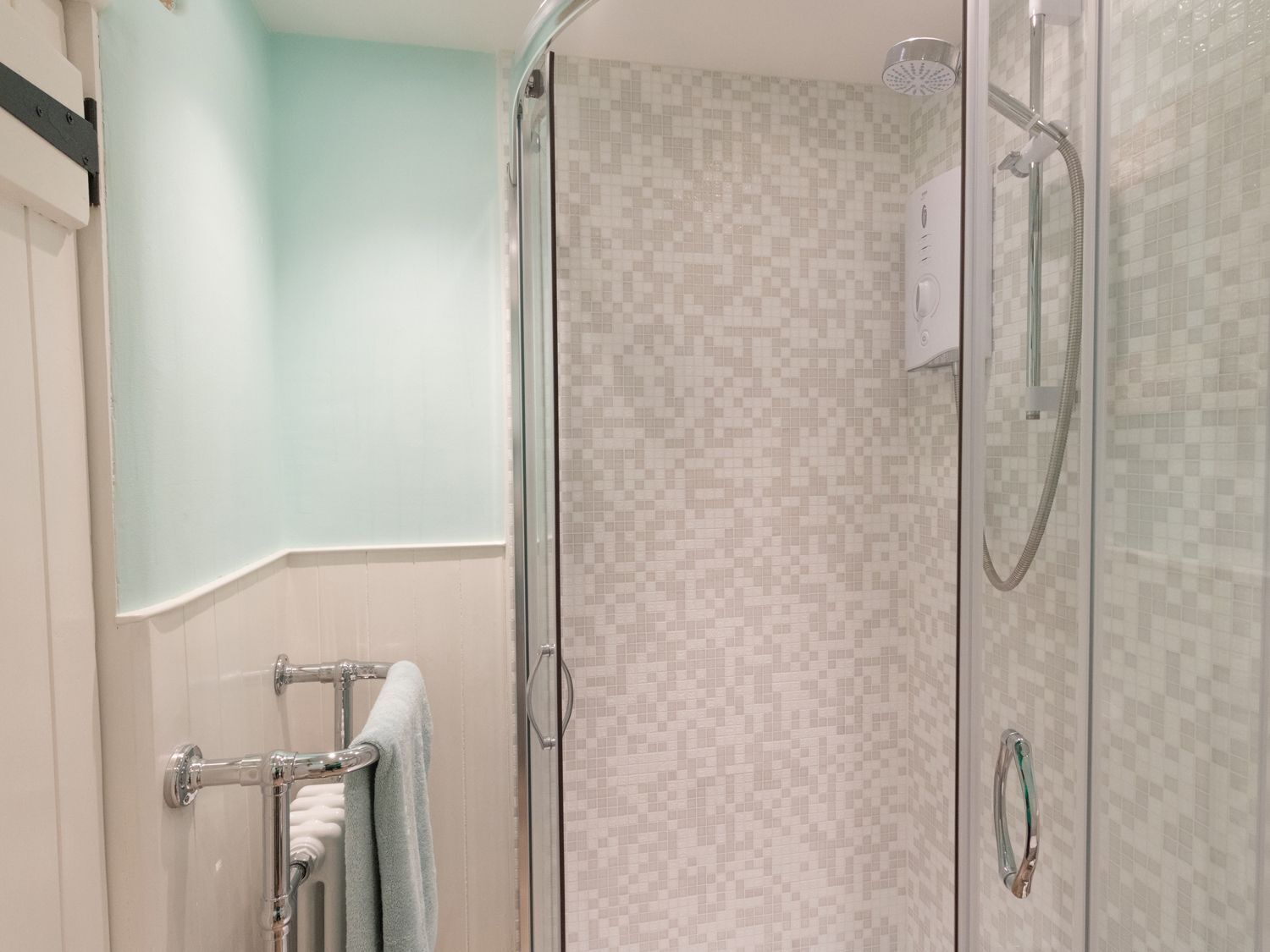 A glass-enclosed shower with a tiled wall, a towel rack, and a shower control panel.