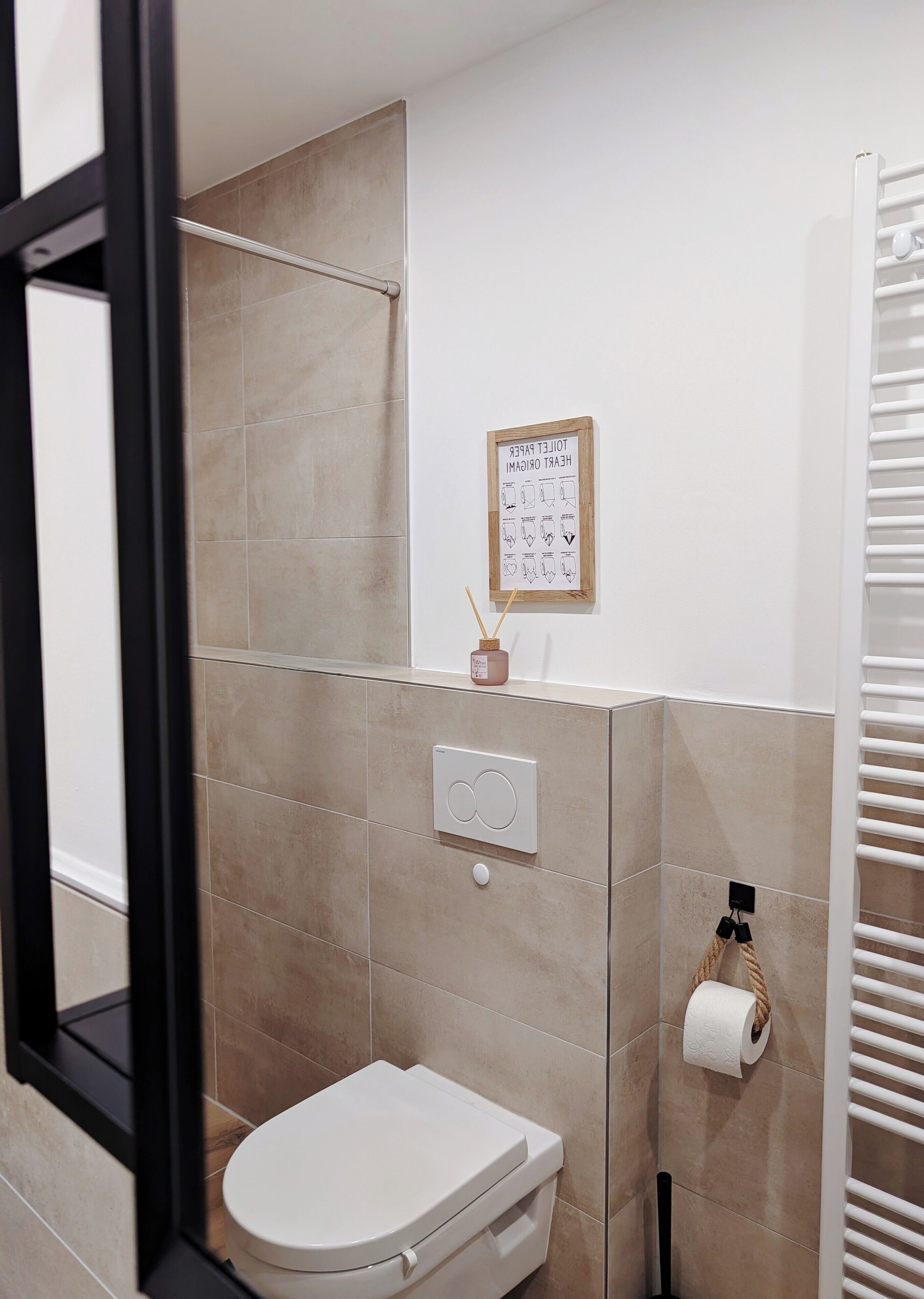 Een badkamer met toilet, handdoekhouder, toiletrolhouder en een bordje in een lijst aan de muur.