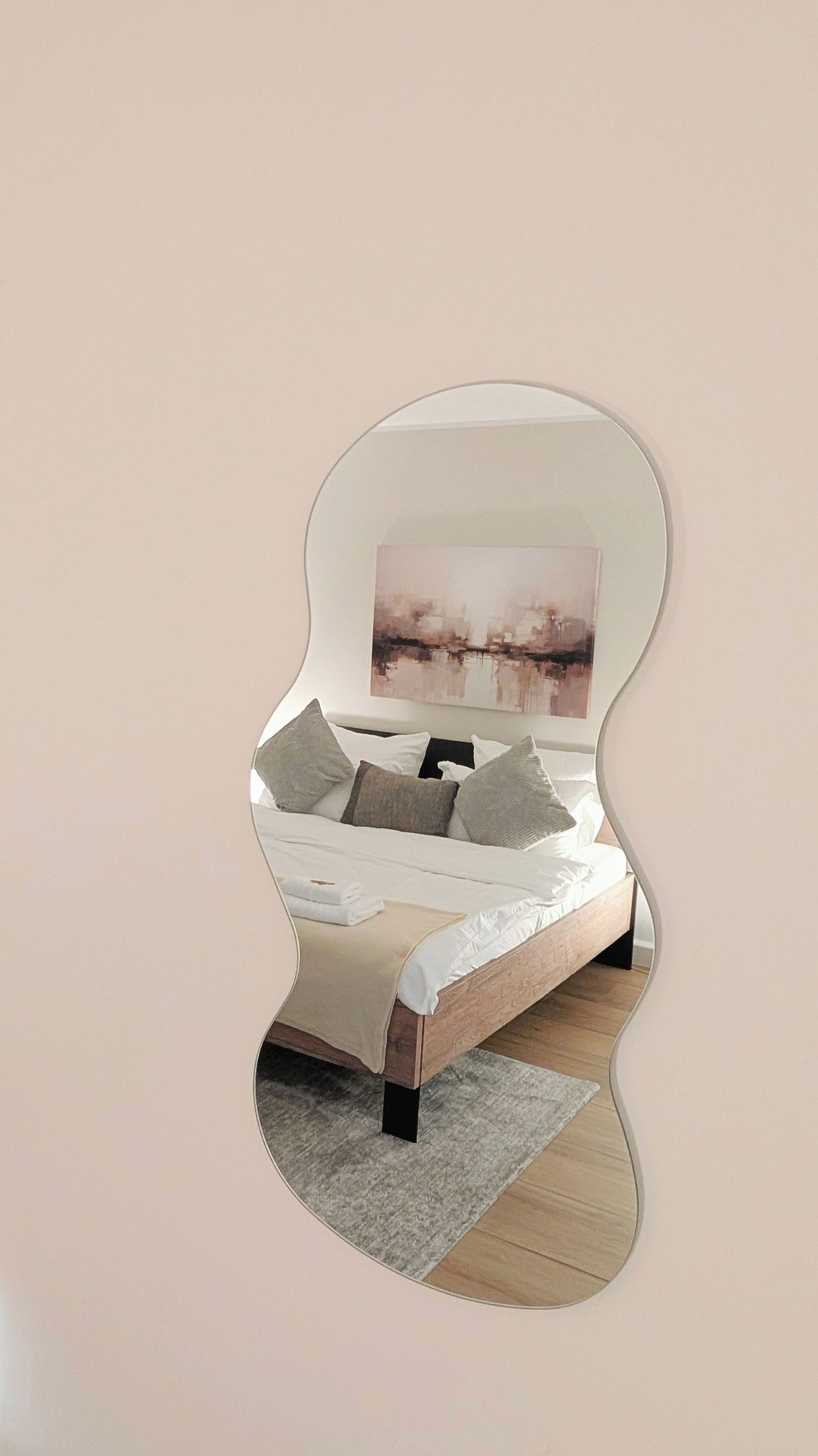 A bedroom with a bed, pillows, a rug, and a wall-mounted mirror reflecting the room.