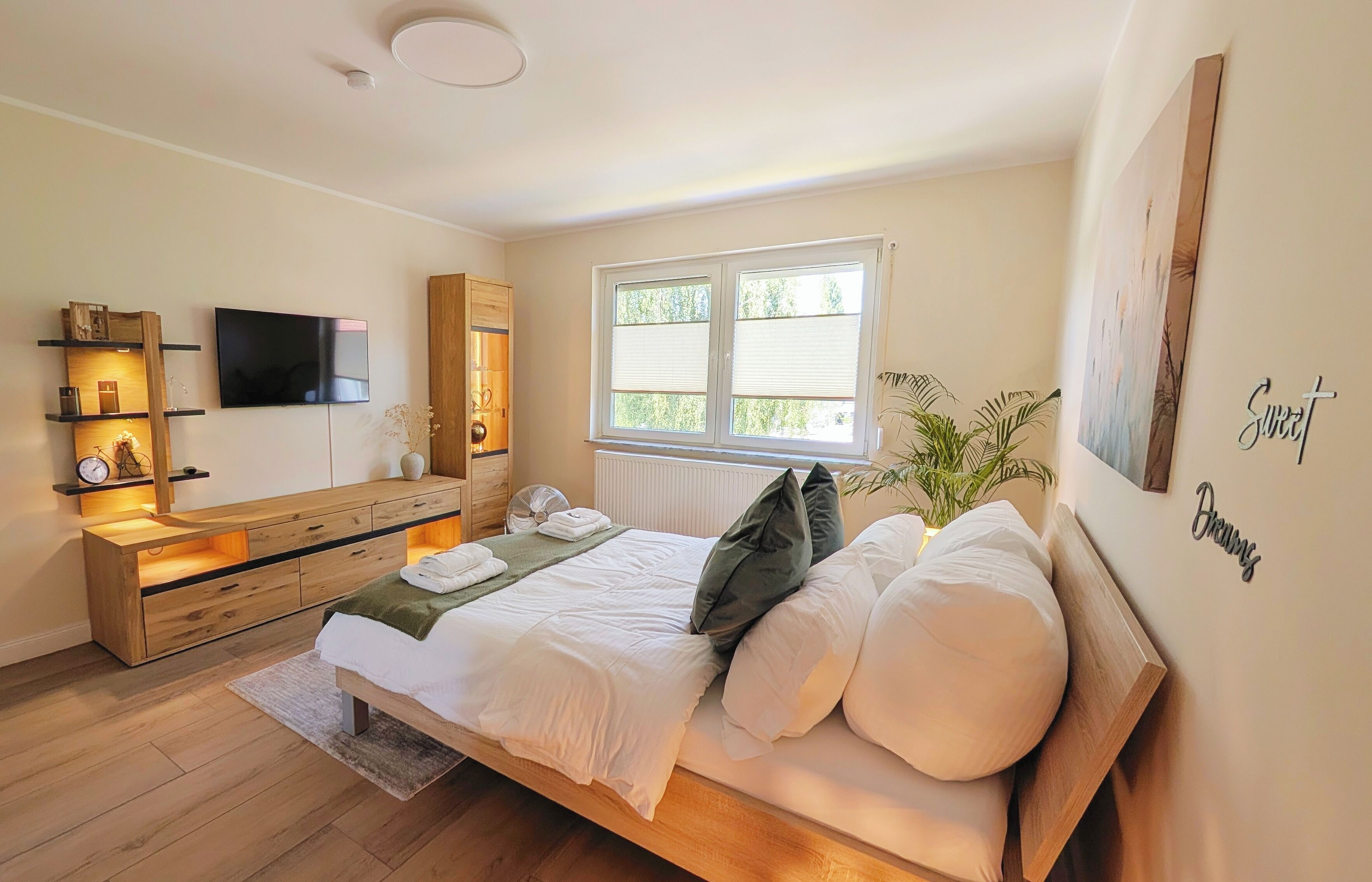 A bedroom with a bed, bedside table, TV, window, and a wall with a sign.