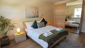Quarto com cama, mesa de cabeceira com luminária, planta em vaso, obra de arte e espelho.