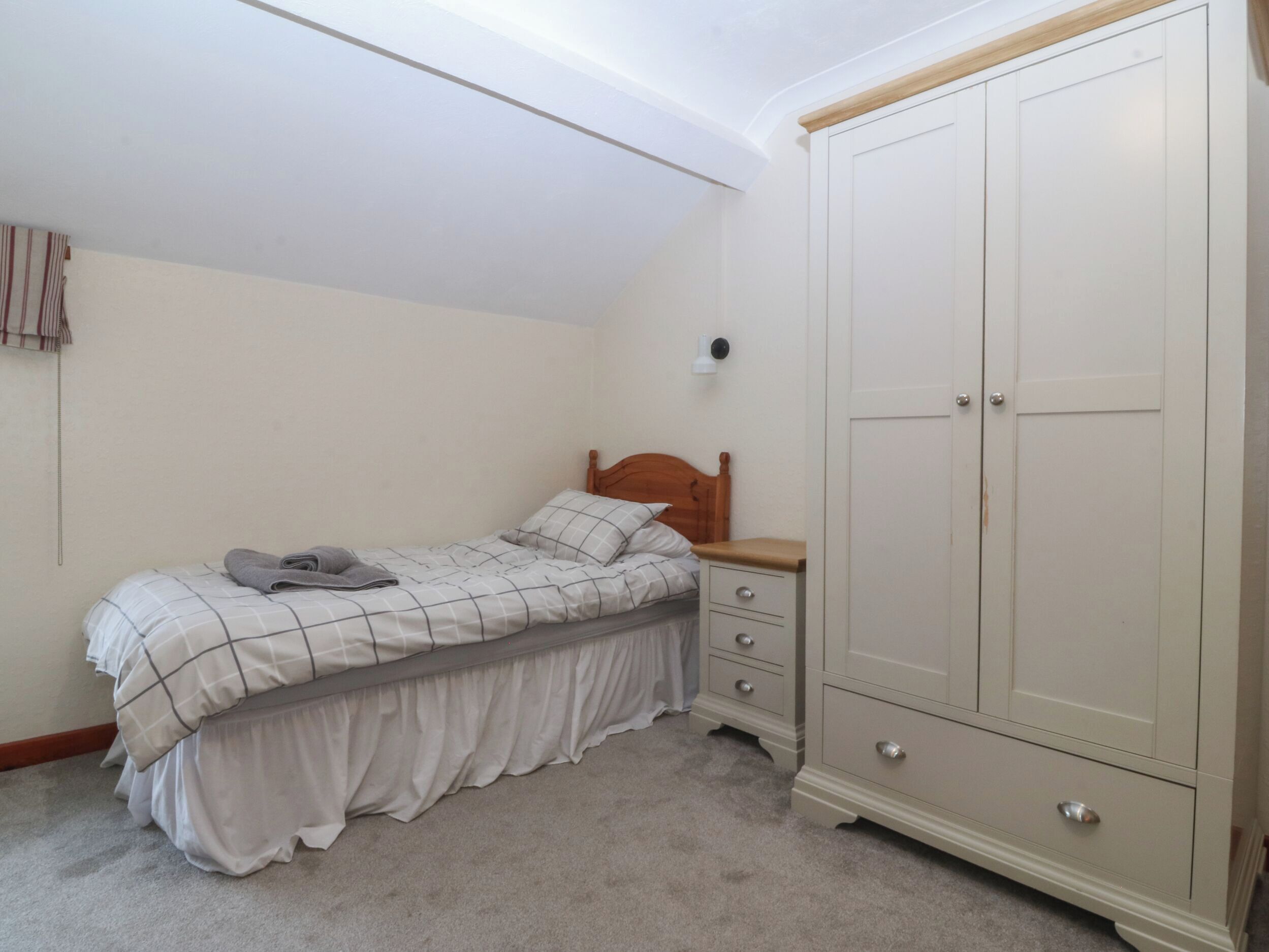 Un dormitorio con una cama individual, una mesita de noche, un armario y una lámpara fijada a la pared.
