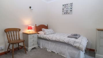 Un dormitorio con cama, una silla, una mesita de noche con lámpara, una obra de arte en la pared y piso alfombrado.
