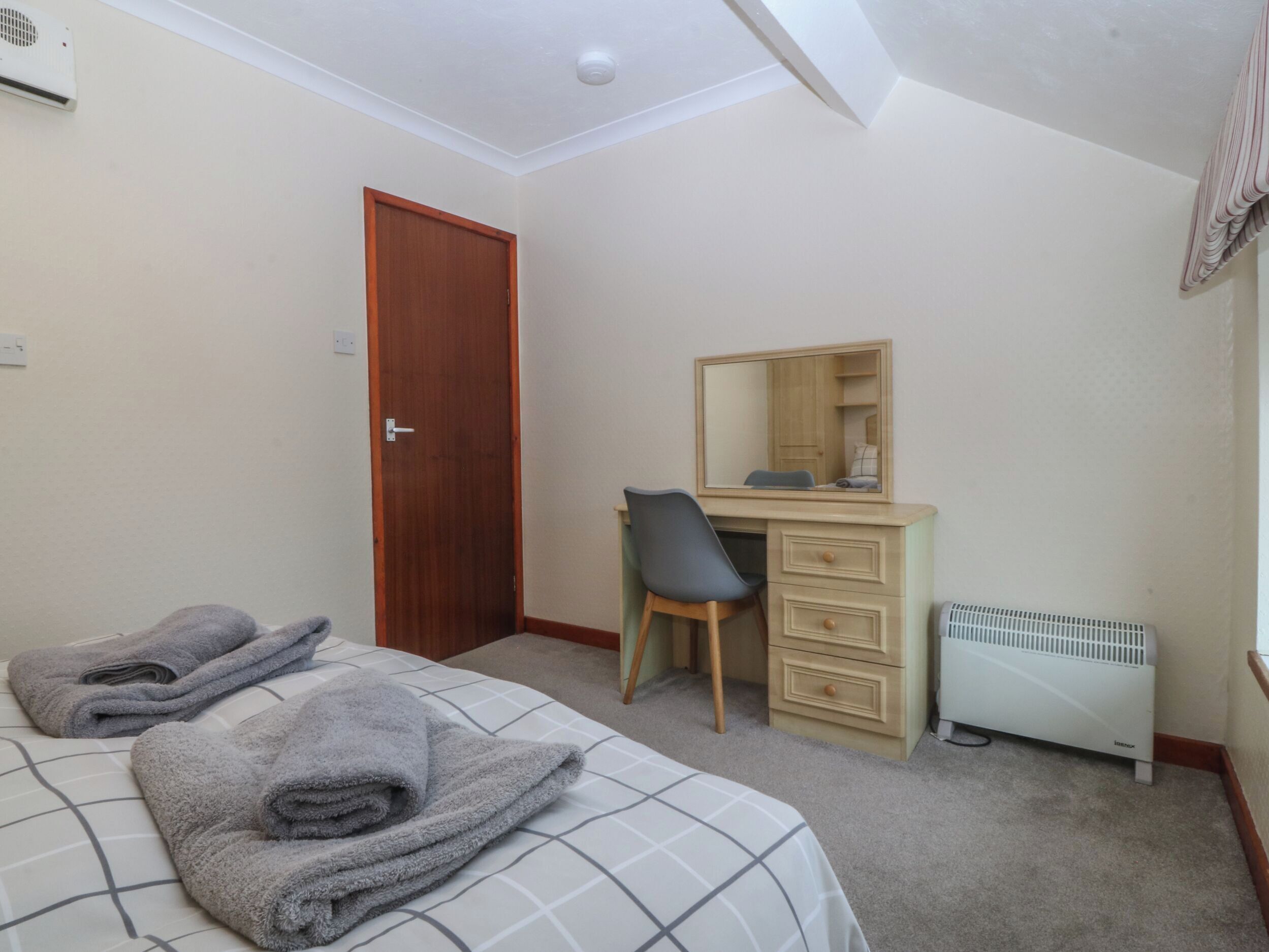 A bedroom with a bed, a desk, a chair, a dresser, a radiator, and a door.