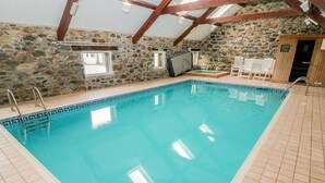 Ein Hallenbad mit Steinwänden und Holzbalken, gefliester Boden und einige Stühle.
