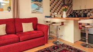 Una sala de estar moderna con un sofá rojo, una cocina con salpicadero de azulejos y una zona de bar con taburetes.