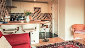 Cocina compacta con una isla central, taburetes de bar y un sofá rojo.