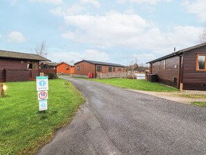 A gravel road leading to a row of wooden cabins with a 'One Way' sign and a '10 mph' speed limit sign. - 12A Lake Escape (Carnforth)