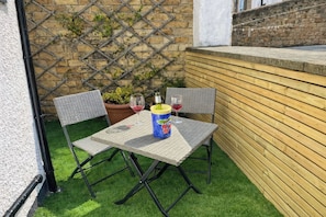 A patio with a table, two chairs, a potted plant, and a bottle of wine. - Number Ten (Morpeth)