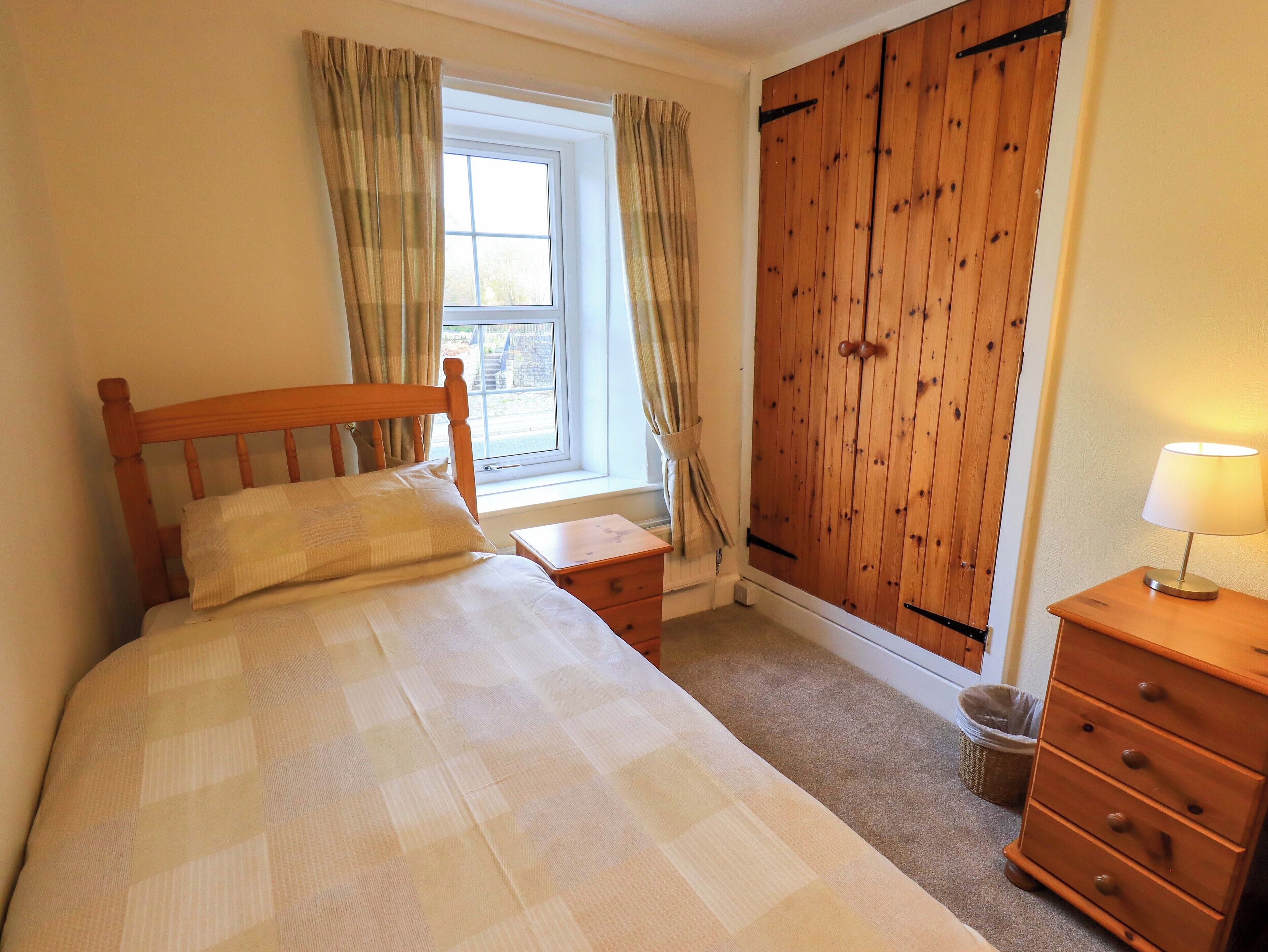 A bedroom with a wooden bed, a nightstand, a dresser, and a window with curtains.