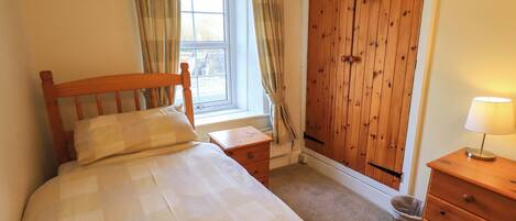 A bedroom with a wooden bed, a nightstand, a dresser, and a window with curtains.