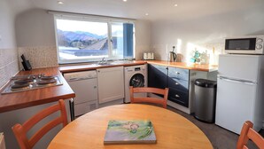 Une cuisine compacte avec vue sur les montagnes, comprenant un lave-linge, un four à micro-ondes et une table à manger avec des chaises.