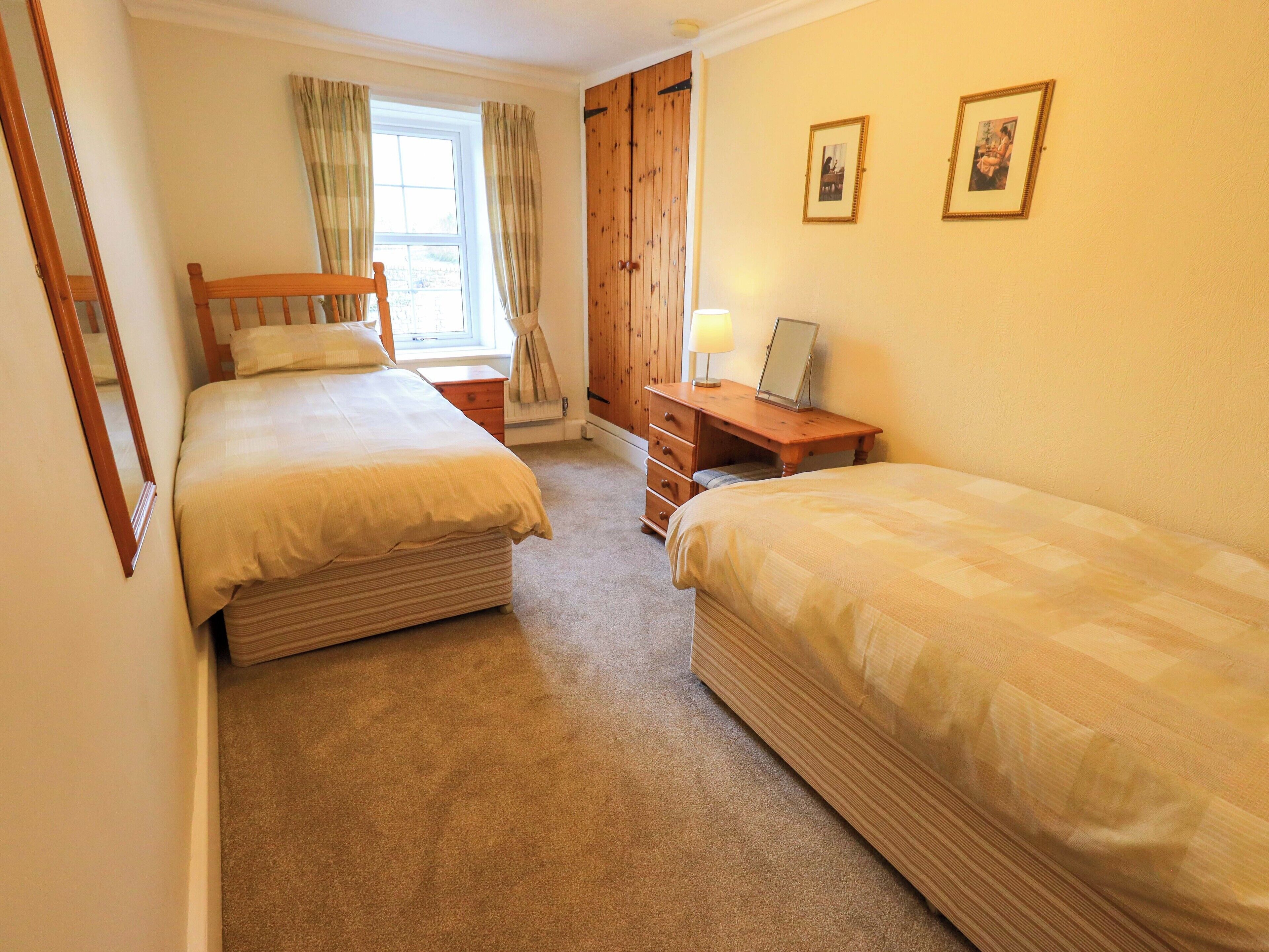 A bedroom with two single beds, a wooden dresser, a desk with a lamp, and a wardrobe.