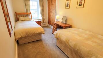 A bedroom with two single beds, a wooden dresser, a desk with a lamp, and a wardrobe.