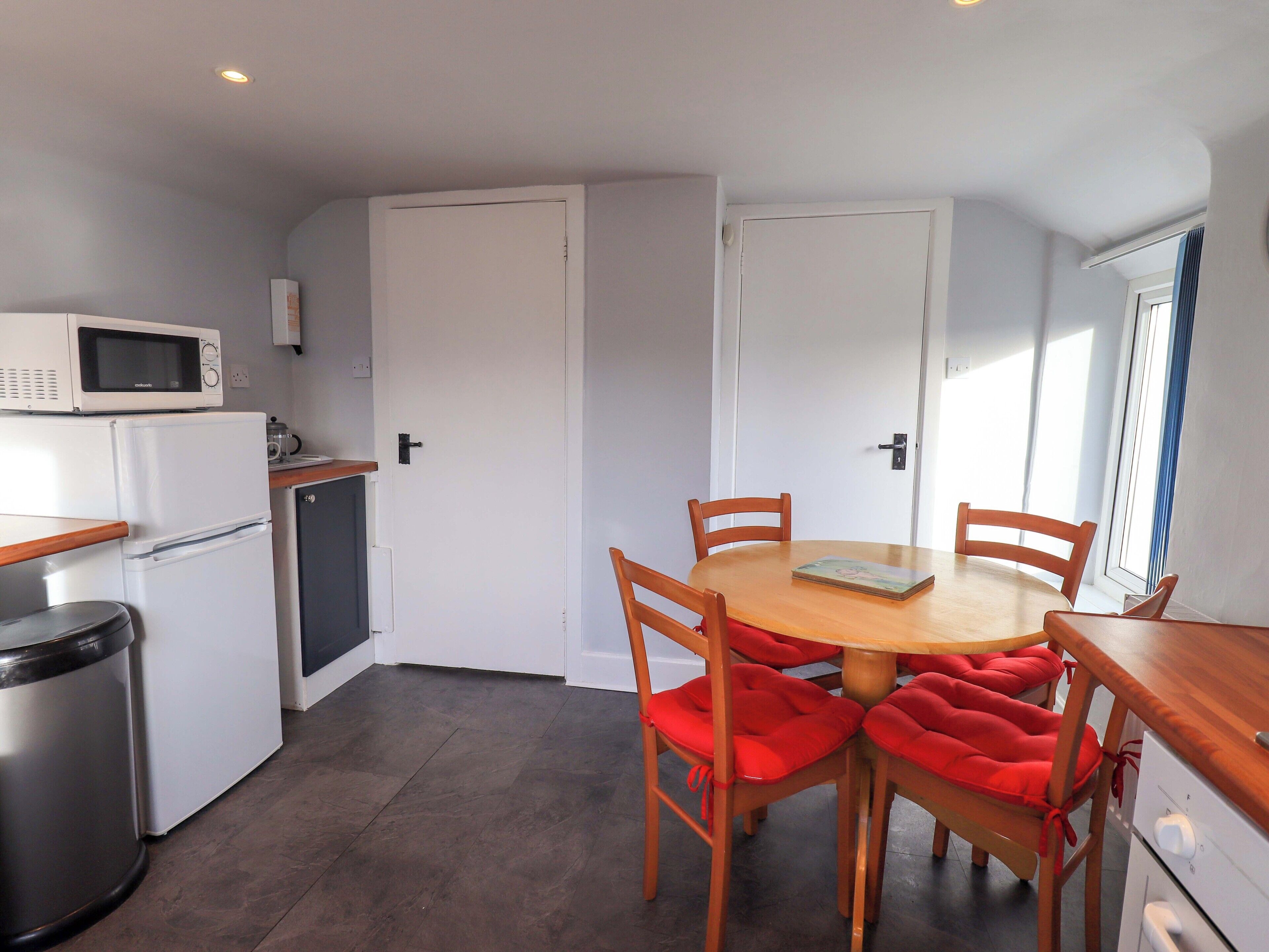 A compact kitchen with a microwave, refrigerator, and sink. There is a dining table with four chairs and a book on it.
