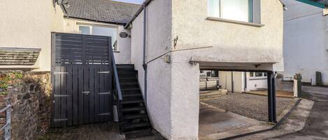 Une maison à deux étages avec un garage, un escalier menant à l’étage supérieur et un petit espace extérieur doté d’un sol en béton.