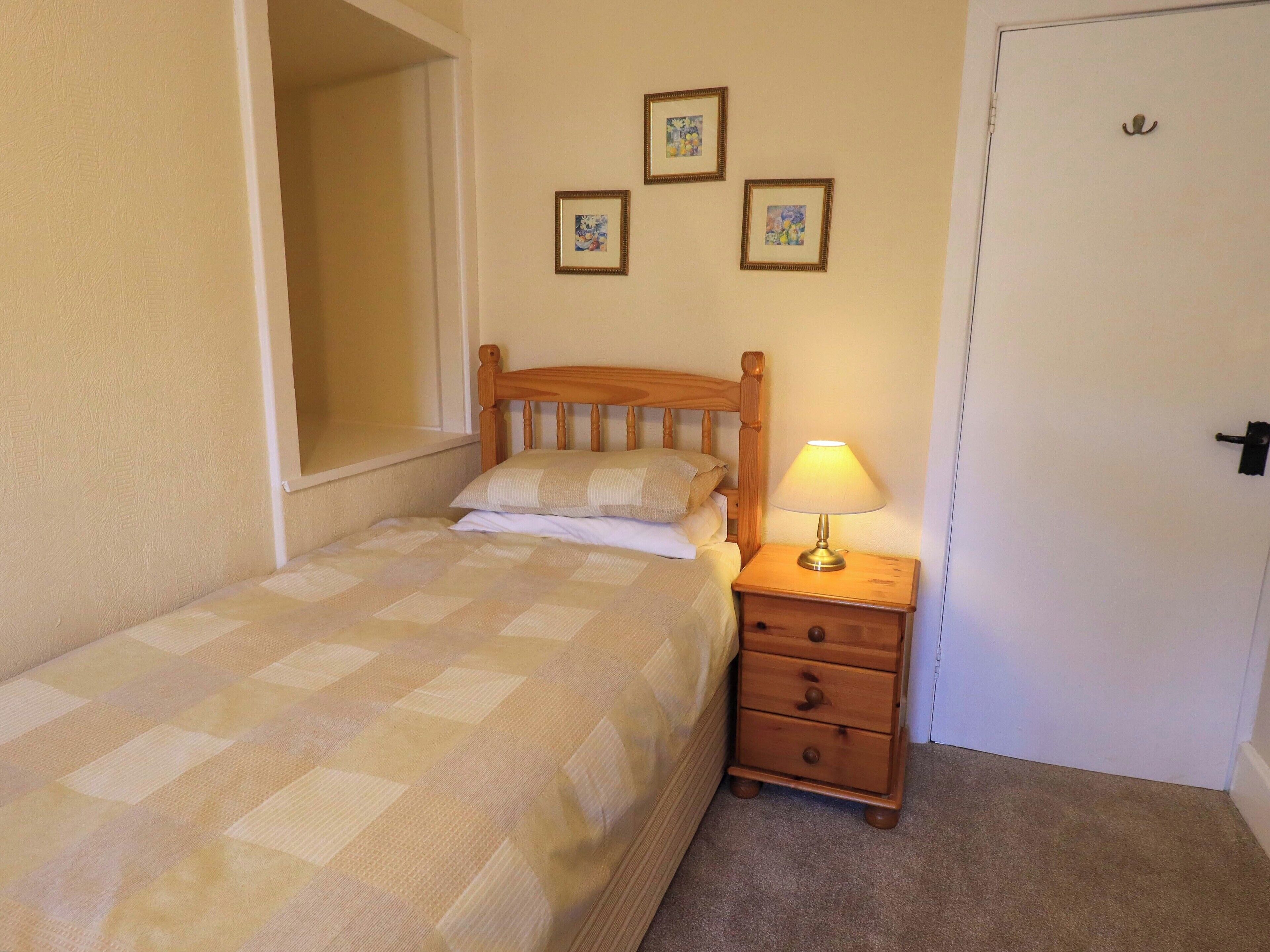 A single bed with a wooden headboard, a bedside table with a lamp, and two framed pictures on the wall.