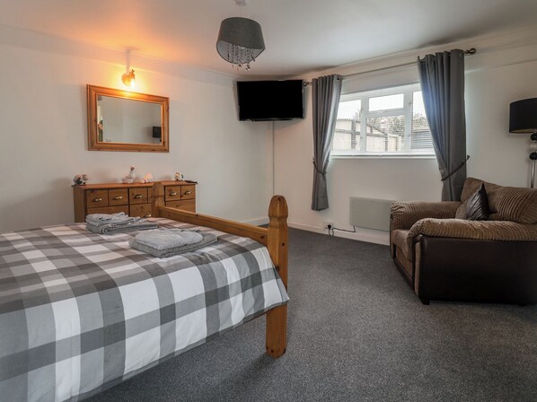 A bedroom with a bed, a wooden dresser, a TV, a chair, and a window with curtains.