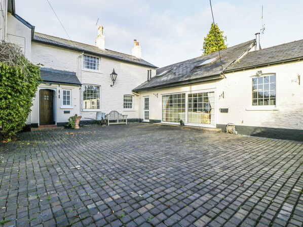 A courtyard with cobblestone paving, a bench, and a white building with multiple windows and doors. - The Coach House (Abergavenny)