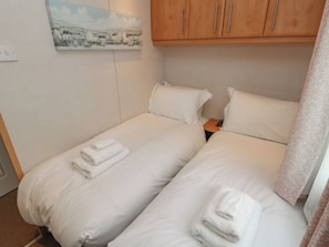 A hotel room with two single beds, white bedding, a painting on the wall, wooden cabinets, and a remote control on the nightstand. - Shorething Getaway (Chichester)