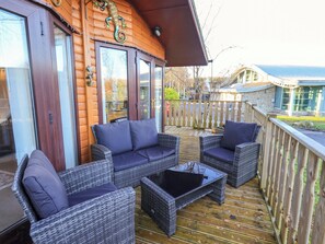 A wooden deck with wicker furniture and a glass door. - Lavender Lodge (Carnforth)