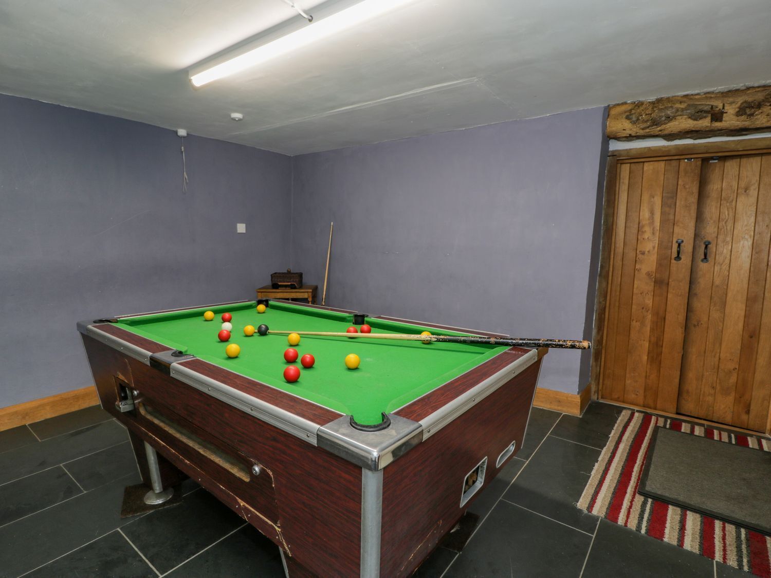 A pool table with balls, a wooden cabinet, and a door with a wooden panel.