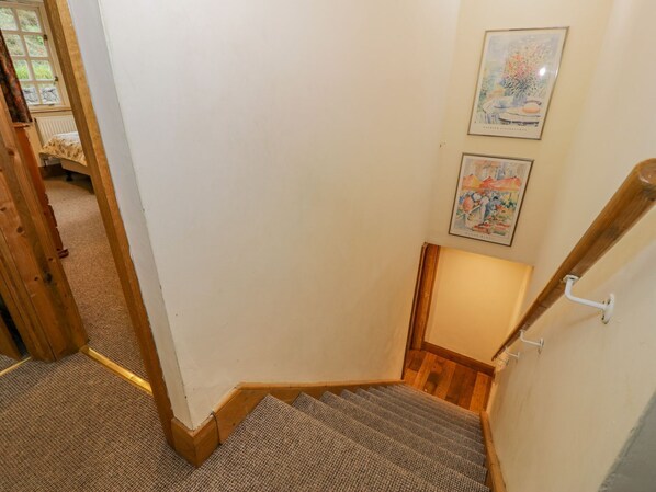 A staircase with a carpeted landing and wooden handrail, leading to a room with a white wall and two framed artworks.