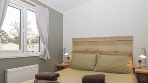 Ein ordentlich bezogenes Bett mit zwei Handtüchern, einem Holz-Kopfteil, Nachttischlampen und einem Fenster mit Vorhängen.