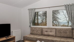 Ein modernes Wohnzimmer mit einer Couch, einem Couchtisch, einem Fernseher und einem Fenster mit Vorhängen.
