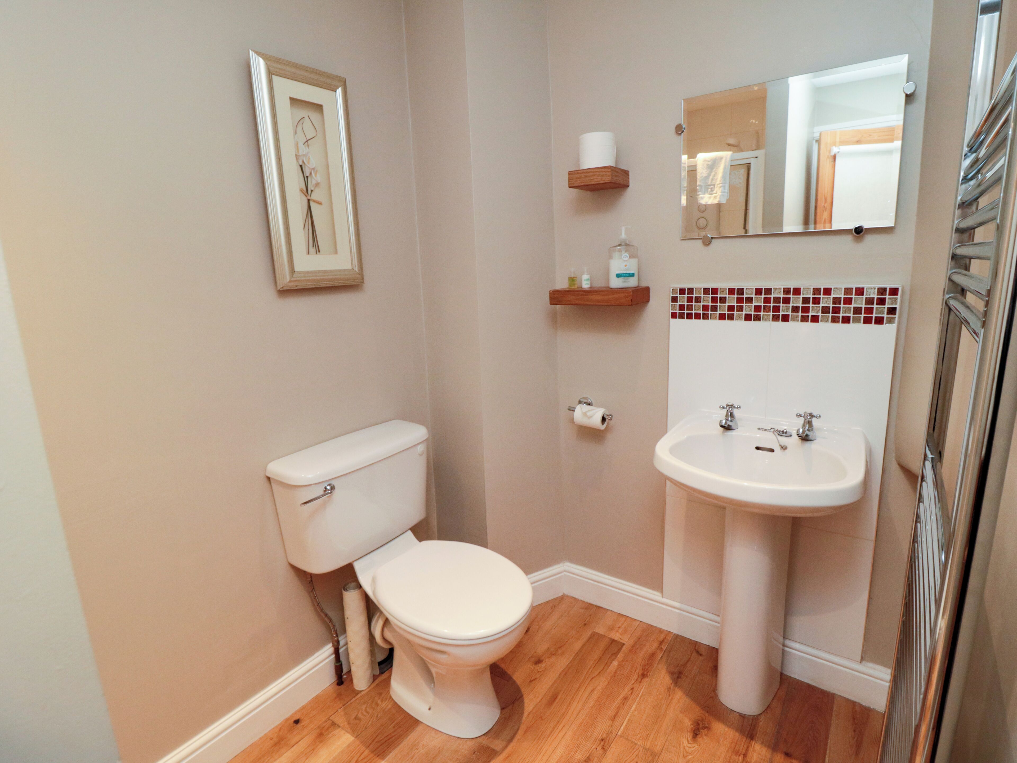 A bathroom with a toilet, sink, framed artwork, and a mirror.