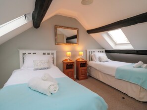 A cozy attic bedroom with two beds, a skylight, a mirror, and two bedside tables with lamps. - The Old Post Office (Pickering)