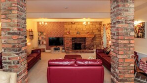 A living room with a brick fireplace, leather sofas, and a television. - The Old Post Office (Pickering)