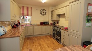 A kitchen with wooden flooring, white cabinets, a clock, and a stove. - The Old Post Office (Pickering)