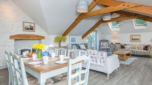 A dining area with a wooden table set for four, surrounded by white chairs with woven seats. - Leeward Cottage (Pembroke)