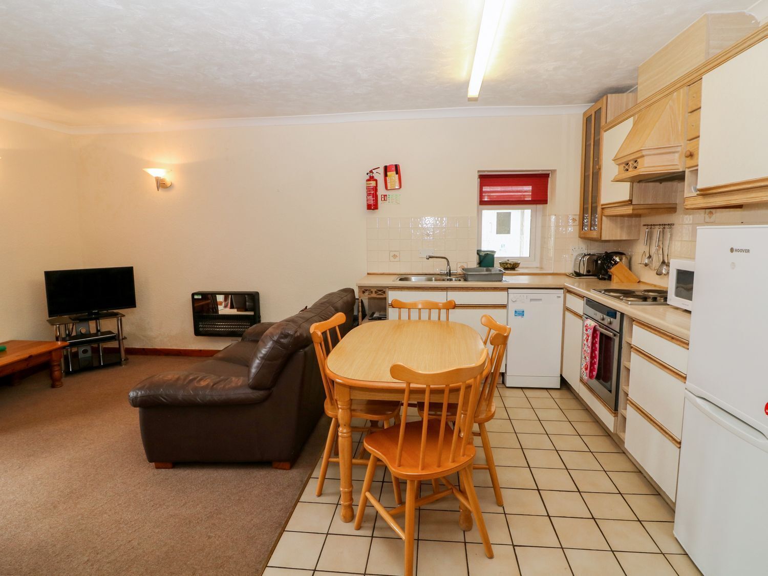 A compact living space with a sofa, a dining table with chairs, a kitchen area with a refrigerator, stove, and microwave, and a television in the corner.