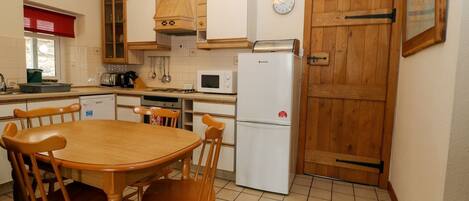 A compact kitchen with wooden cabinets, a microwave, a refrigerator, and a dining table with chairs.