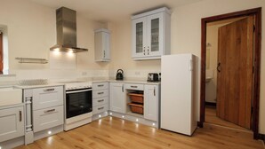 A modern kitchen with white cabinetry, a stainless steel range hood, a built-in oven, and a refrigerator. - Walton Maisonette (Craven Arms)