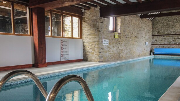 An indoor swimming pool with stone walls, a no running, no driving, no dogs, no ball games, and no unaccompanied children sign. - Walton Maisonette (Craven Arms)